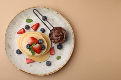 Delicious pancakes served with berries and chocolate spread on beige background, top view. Space for text