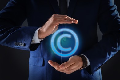 Image of Man holding virtual icon of copyright symbol on dark background, closeup