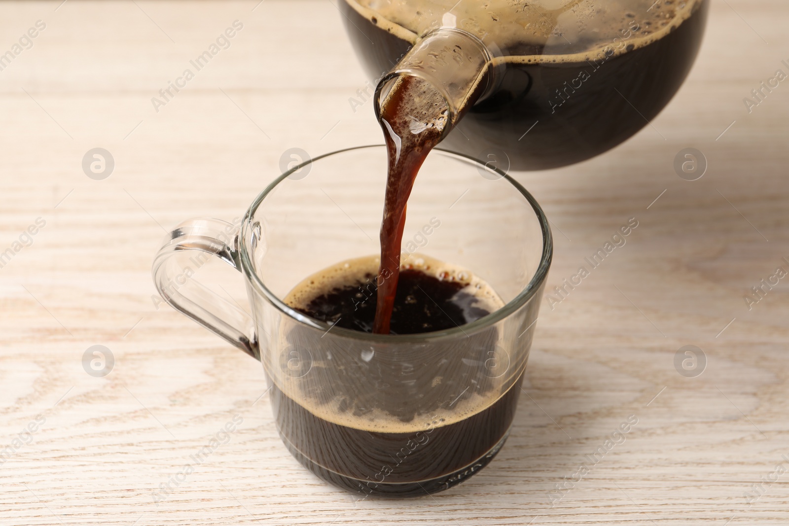 Photo of Pouring coffee into cup at light wooden table, closeup