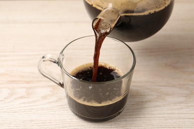 Photo of Pouring coffee into cup at light wooden table, closeup