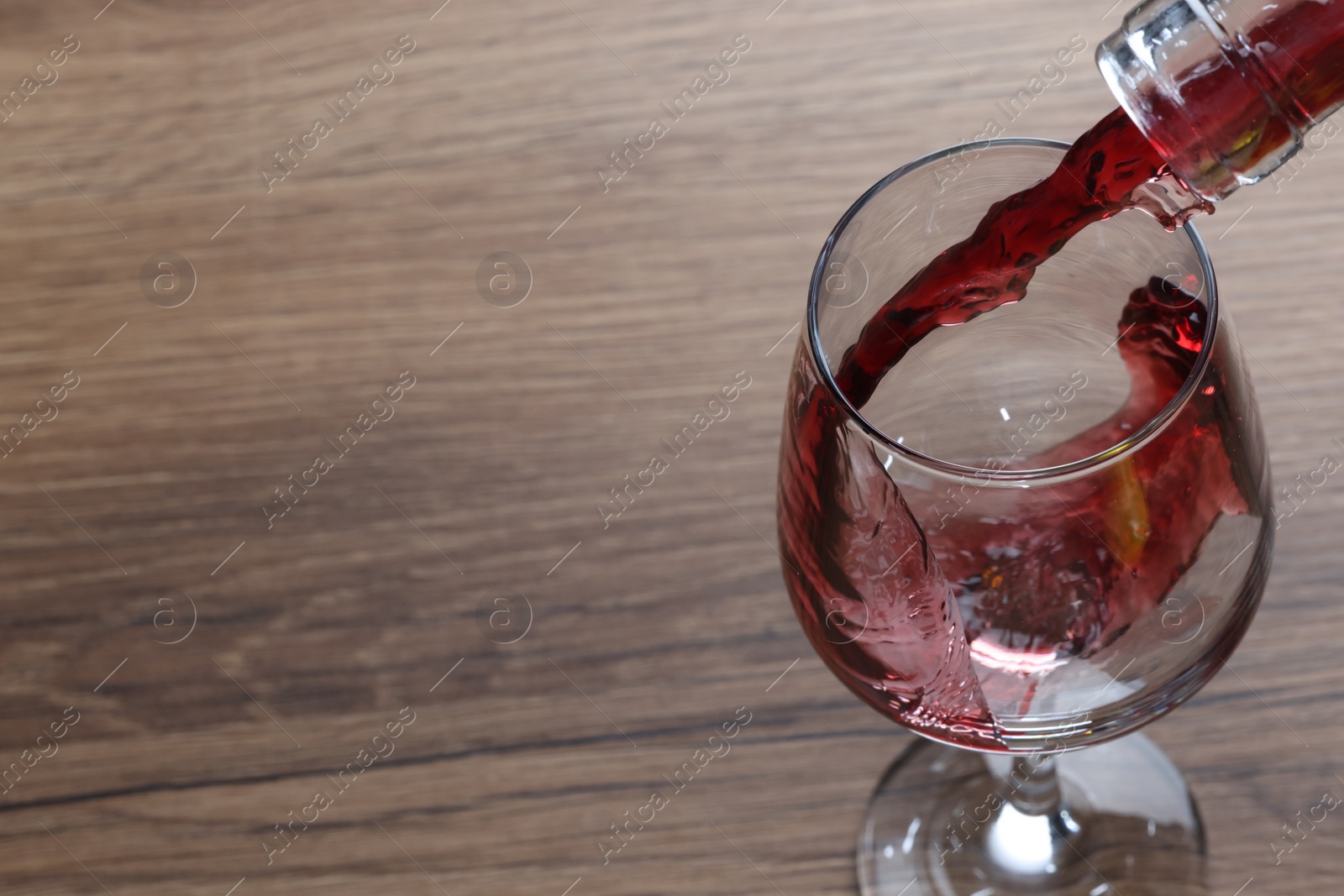 Photo of Pouring tasty red wine in glass at wooden table, closeup. Space for text