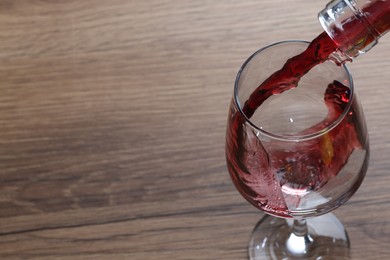 Pouring tasty red wine in glass at wooden table, closeup. Space for text