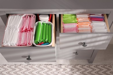 Open cabinet drawers with menstrual pads, tampons and pantyliners indoors, above view