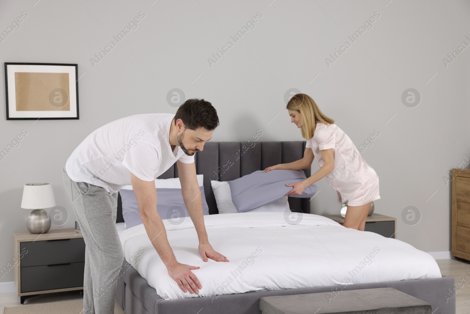 Photo of Couple changing bed linens in room. Domestic chores