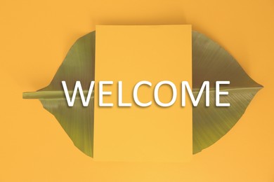 Image of Green banana leaf and word WELCOME on orange background, top view