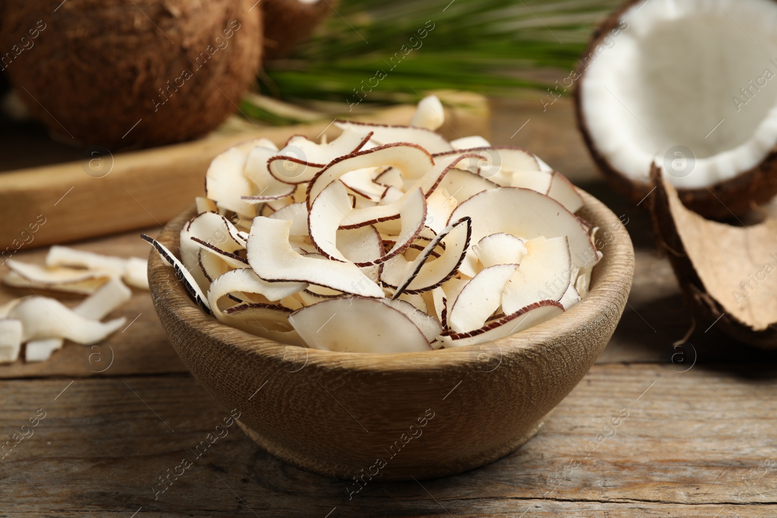 Photo of Tasty coconut chips in bowl on wooden table