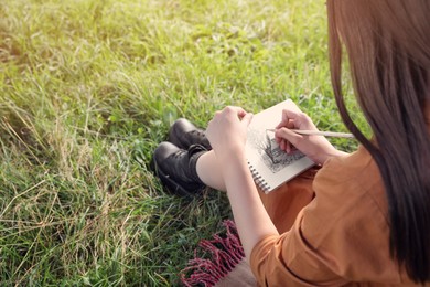 Photo of Beautiful young woman drawing with pencil in notepad outdoors on sunny day, closeup