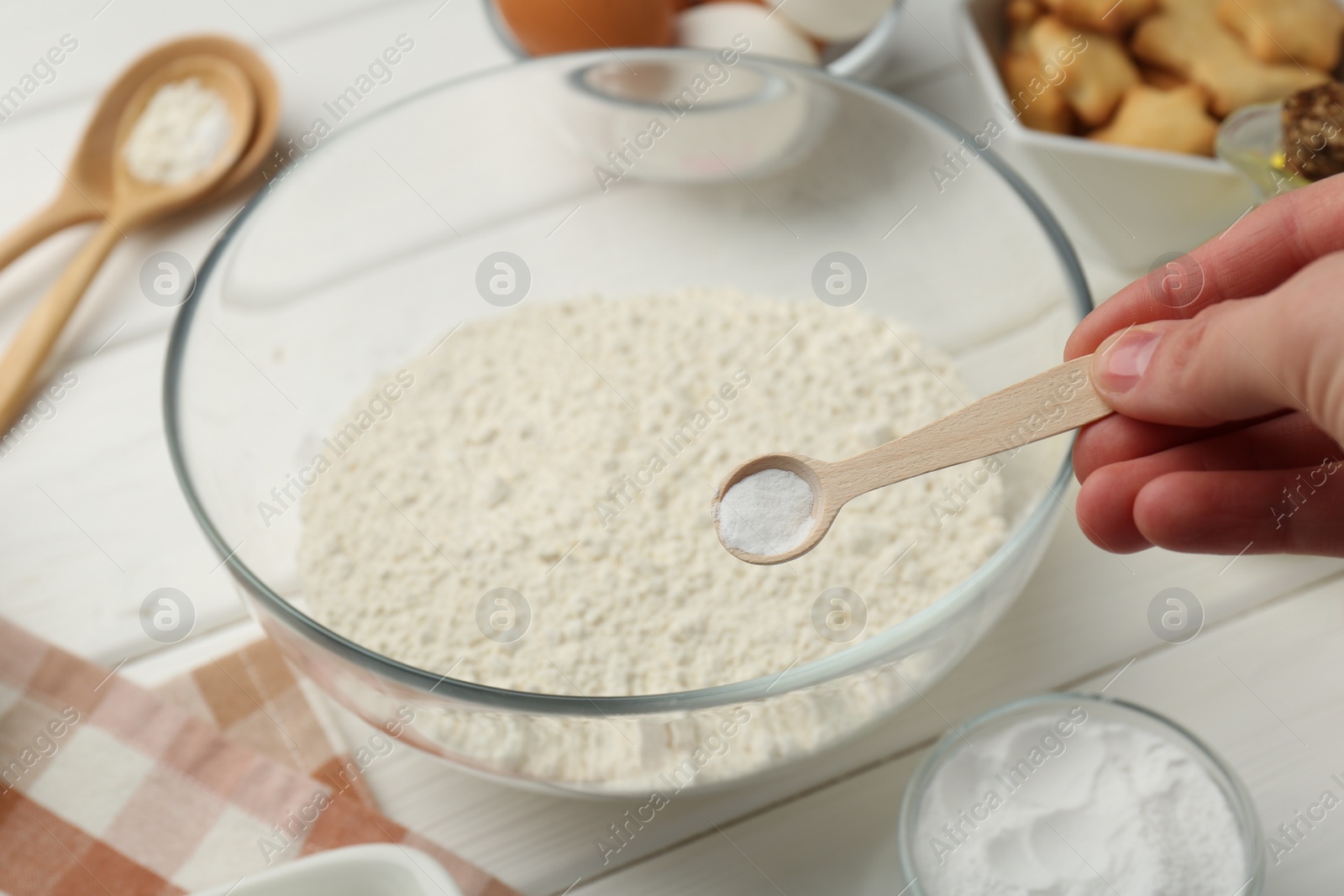 Photo of Woman taking spoon with baking powder from bowl at white wooden table, closeup