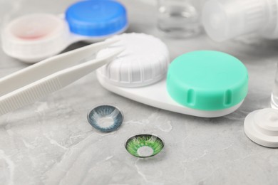 Photo of Different color contact lenses, tweezers and case on light grey marble table, closeup