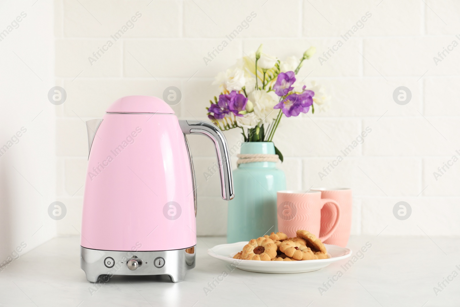 Photo of Modern electric kettle, bouquet, cookies and cups on counter in kitchen