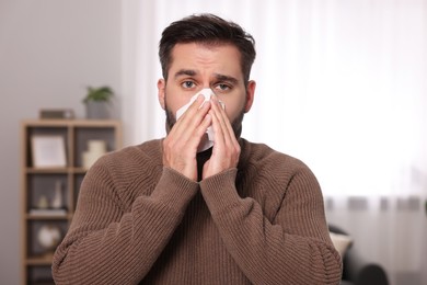 Photo of Sick man with tissue blowing nose at home. Cold symptoms