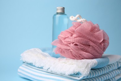 Pink shower puff, bottle of cosmetic product and towel on light blue background, closeup. Space for text