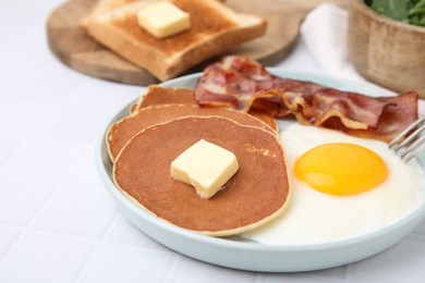 Photo of Tasty pancakes served with fried egg and bacon on white tiled table, closeup
