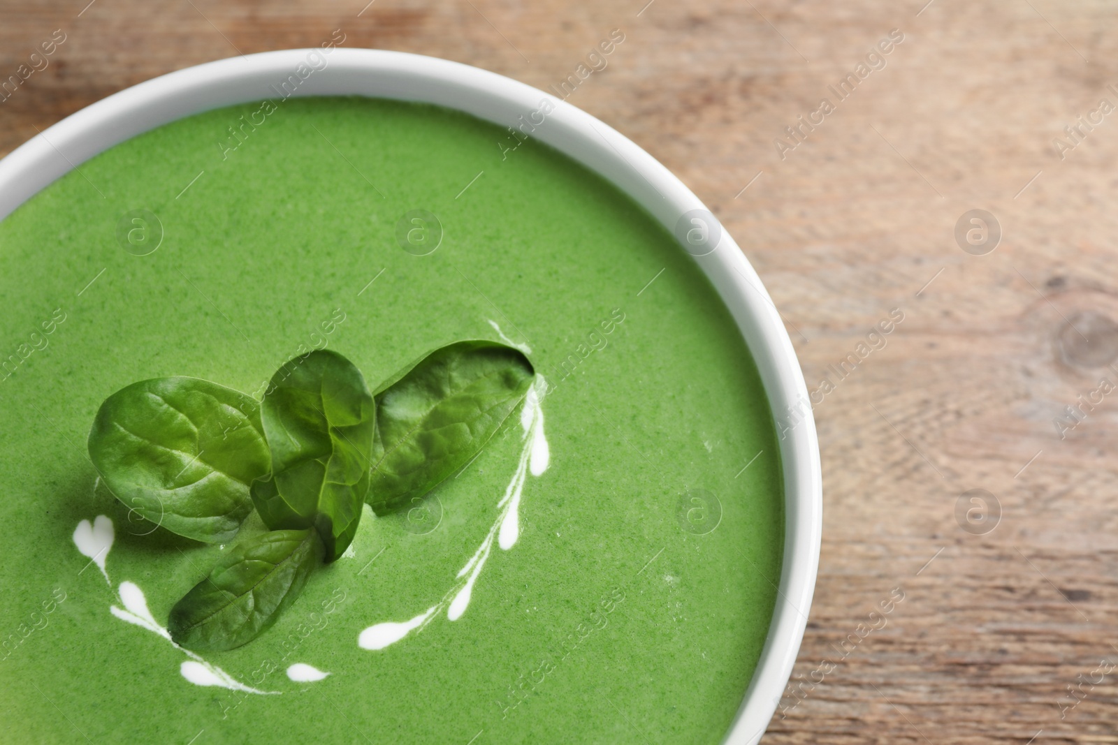 Photo of Bowl of healthy green soup with fresh spinach on wooden table, top view