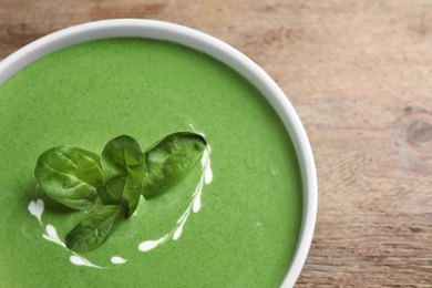 Bowl of healthy green soup with fresh spinach on wooden table, top view