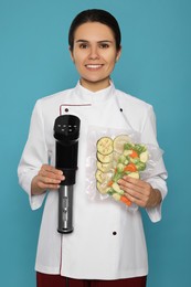 Photo of Chef holding sous vide cooker and vegetables in vacuum packs on light blue background