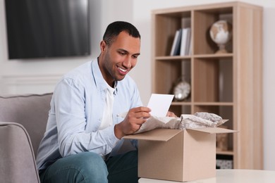 Happy man with greeting card near parcel at home. Internet shopping