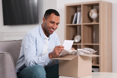 Photo of Happy man with greeting card near parcel at home. Internet shopping