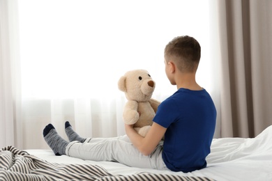 Lonely little boy sitting on bed in room. Autism concept