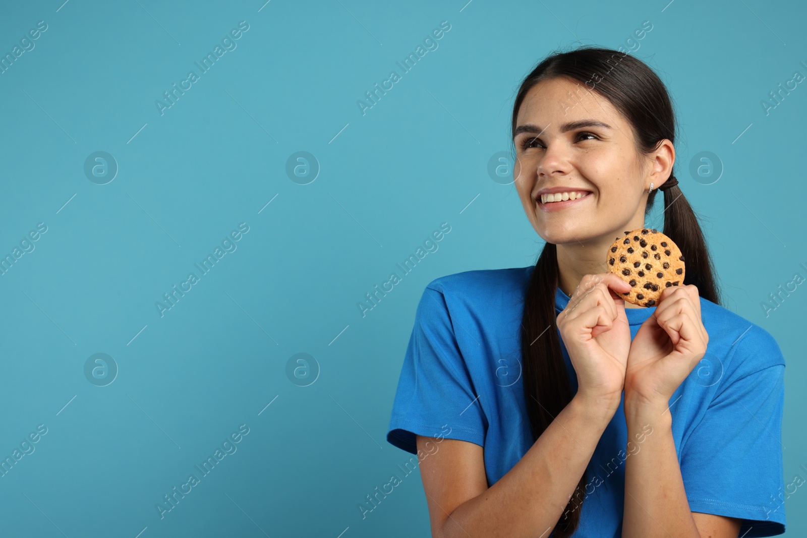 Photo of Young woman with chocolate chip cookie on light blue background, space for text
