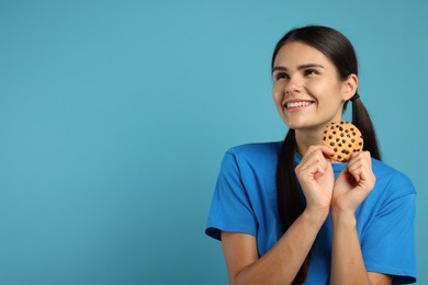 Young woman with chocolate chip cookie on light blue background, space for text