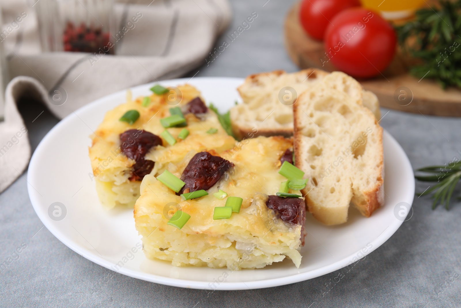 Photo of Tasty sausage casserole with green onion and bread on grey table, closeup