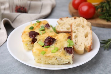 Photo of Tasty sausage casserole with green onion and bread on grey table, closeup