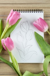 Sketch of tulips in notebook and flowers on wooden table, flat lay