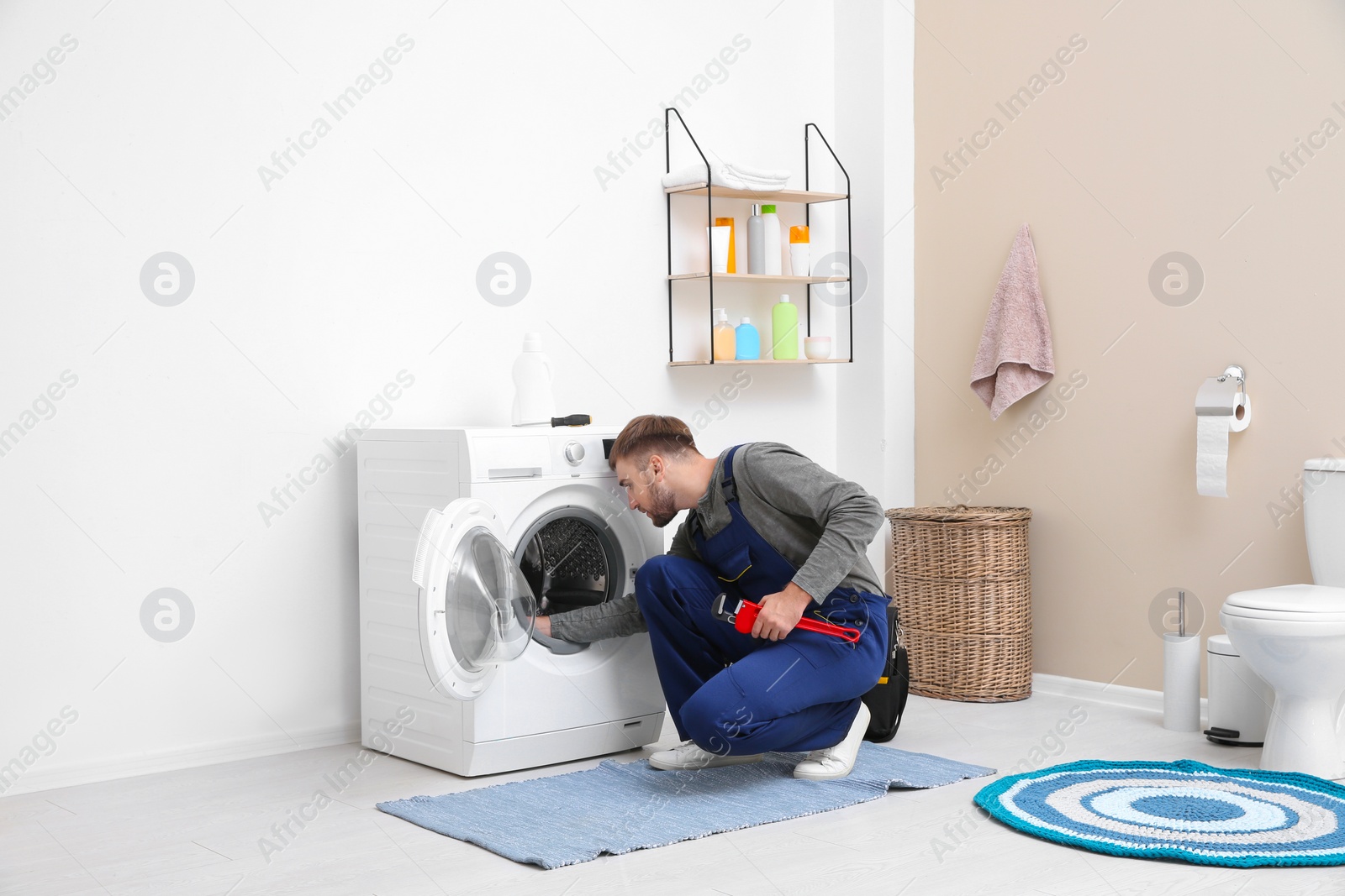 Photo of Young plumber fixing washing machine in bathroom