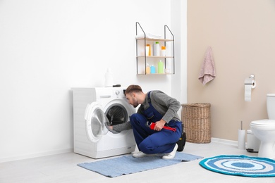 Young plumber fixing washing machine in bathroom