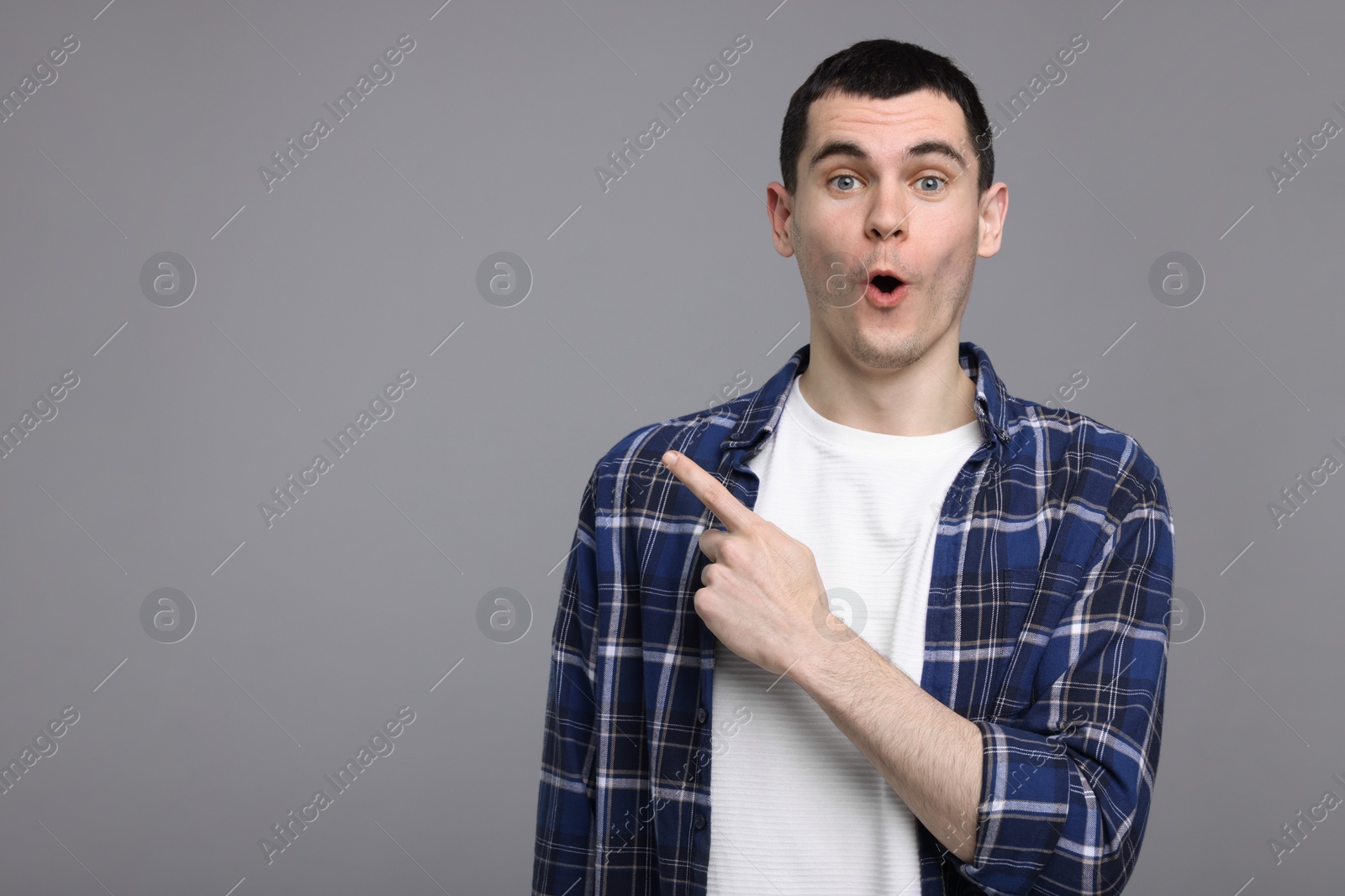 Photo of Surprised man pointing at something on grey background, space for text