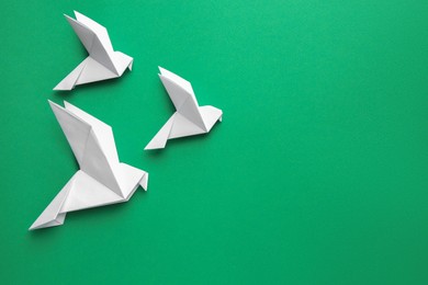 Photo of Beautiful white origami birds on green background, flat lay. Space for text