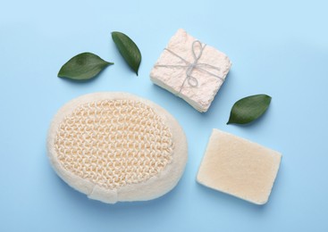 Photo of New sponge, fresh leaves and soap bars on light blue background, flat lay