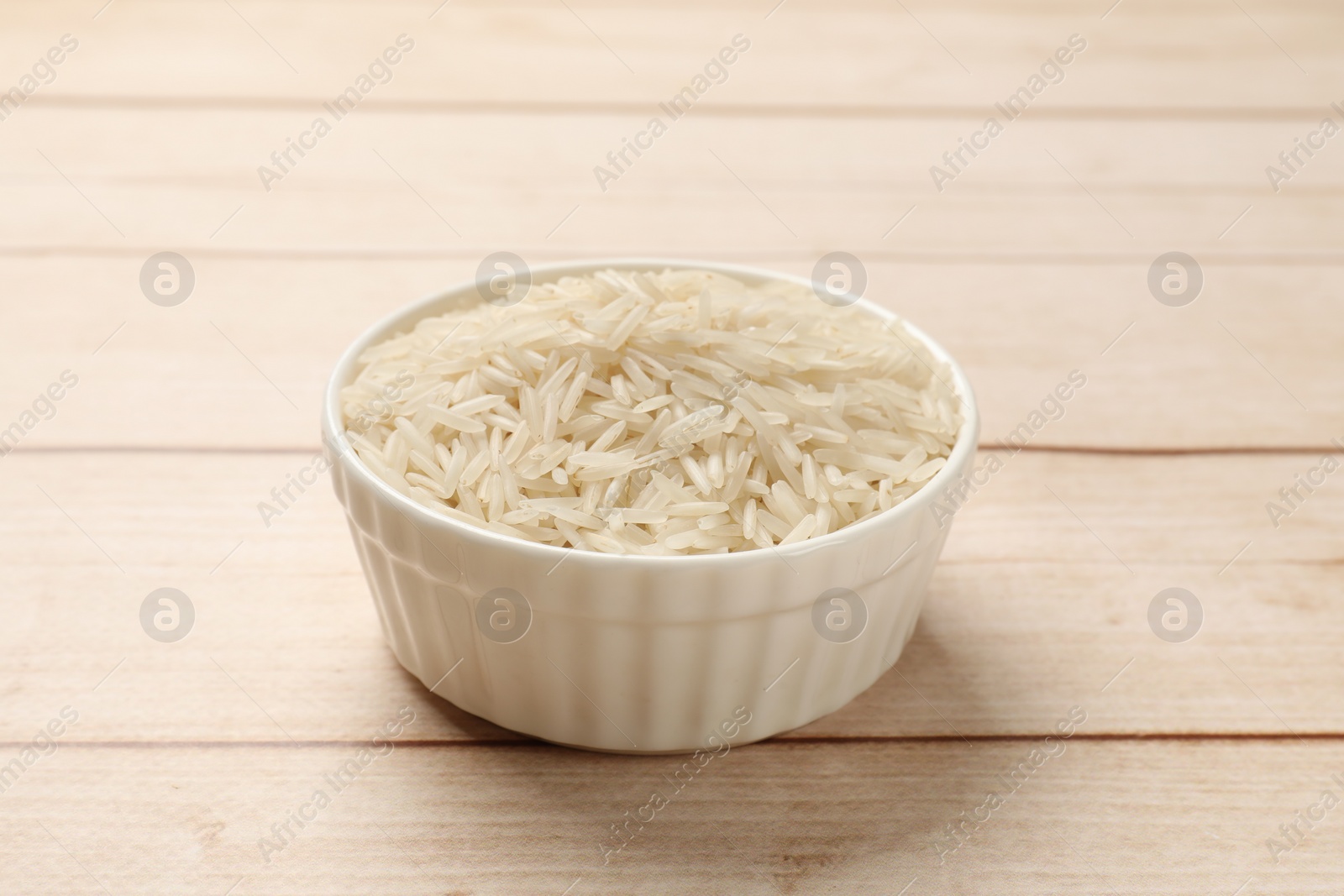 Photo of Raw basmati rice in bowl on white wooden table, closeup