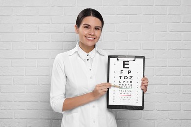 Photo of Ophthalmologist pointing at vision test chart near white brick wall
