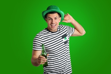 Happy man in St. Patrick's Day outfit with beer on green background