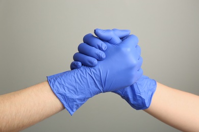 Photo of People in medical gloves shaking hands on grey background, closeup