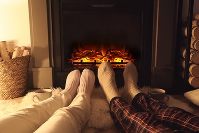 Photo of Couple in knitted socks near fireplace at home, closeup of legs