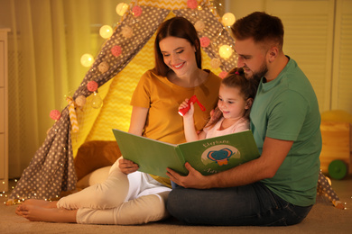 Family with flashlight reading book at home