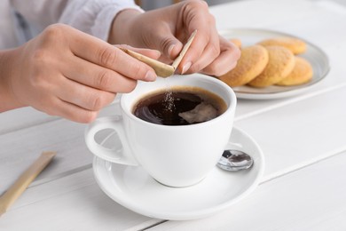 Woman adding sugar to aromatic coffee at white wooden table, closeup