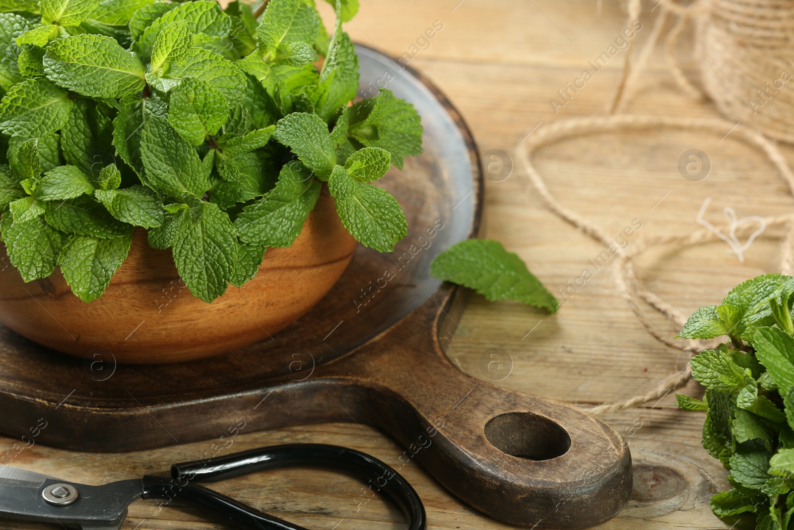 Photo of Bowl with fresh green mint leaves, twine and scissors on wooden table