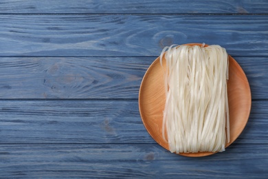 Plate with raw rice noodles on wooden background, top view. Space for text