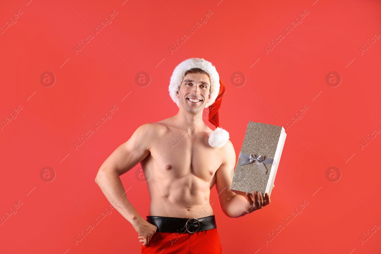 Photo of Young muscular man in Santa hat with gift box on color background