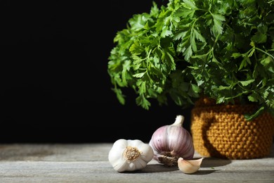 Photo of Fresh raw garlic and parsley on wooden table against black background. Space for text