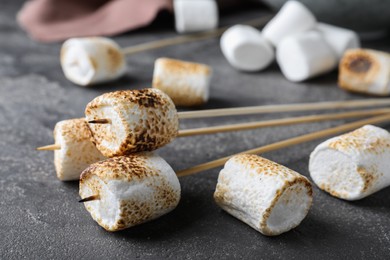 Photo of Sticks with roasted marshmallows on grey table, closeup