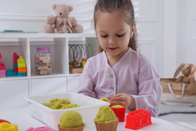 Cute little girl playing with bright kinetic sand at table in room