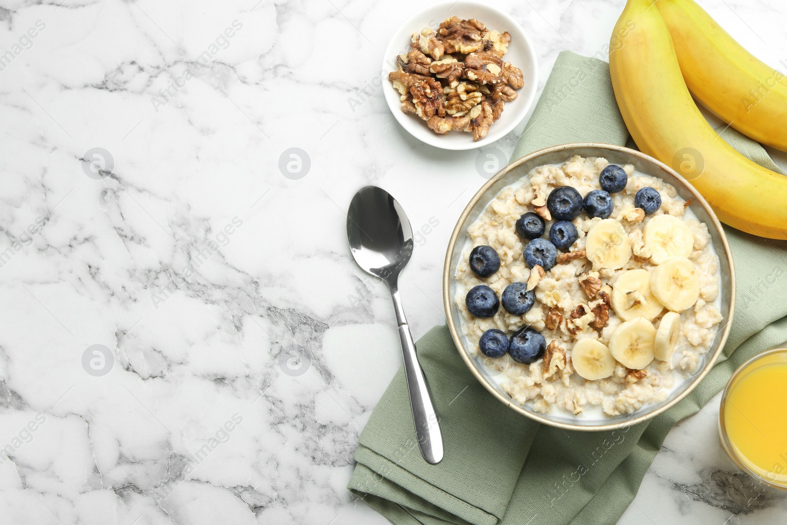 Photo of Tasty oatmeal with banana, blueberries, walnuts and milk served in bowl on white marble table, flat lay. Space for text