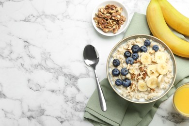 Tasty oatmeal with banana, blueberries, walnuts and milk served in bowl on white marble table, flat lay. Space for text