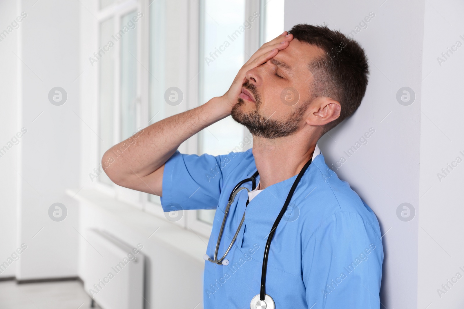 Photo of Exhausted doctor near white wall in hospital hallway