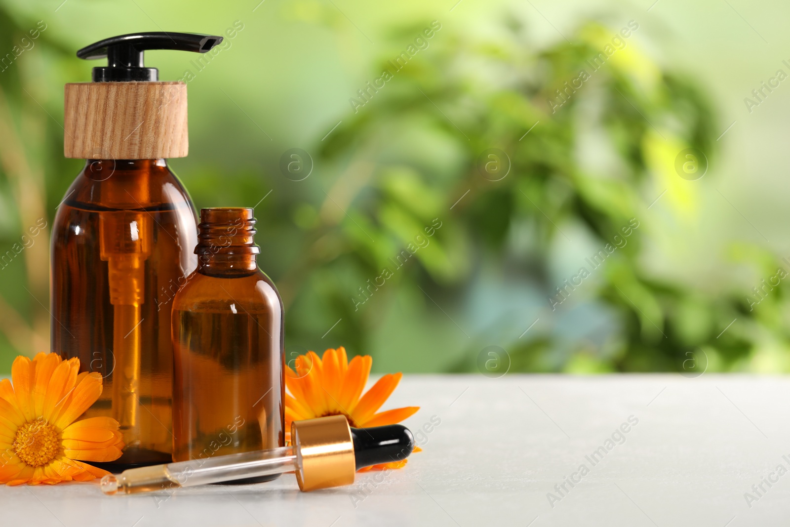 Photo of Bottles of essential oils and beautiful calendula flowers on white table outdoors, space for text